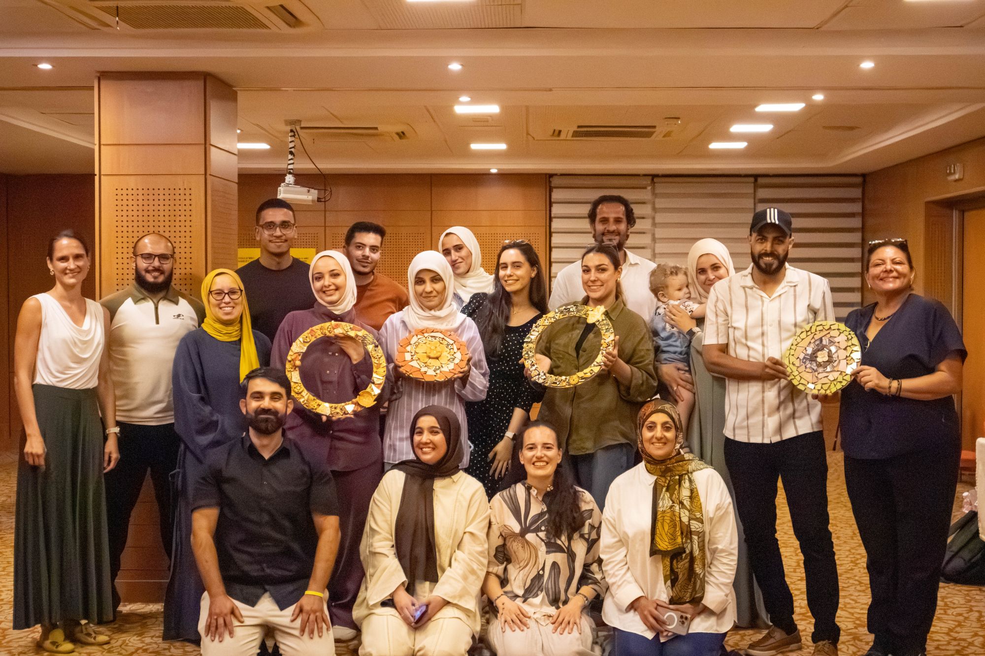 A team of 18 from an international humanitarian organisation holding the mosaics they made together at a Crafted Visions team-building in Tunis